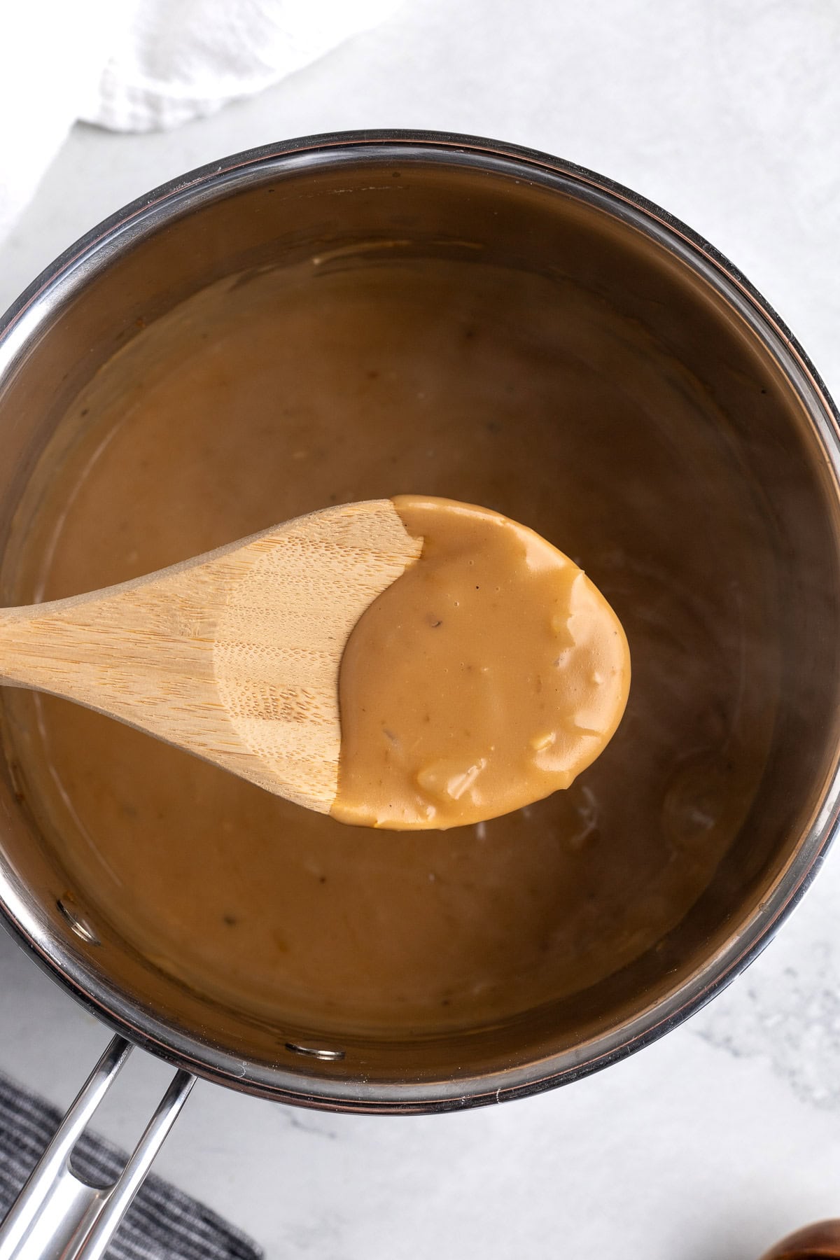 Thick brown gravy coating a wooden spoon.
