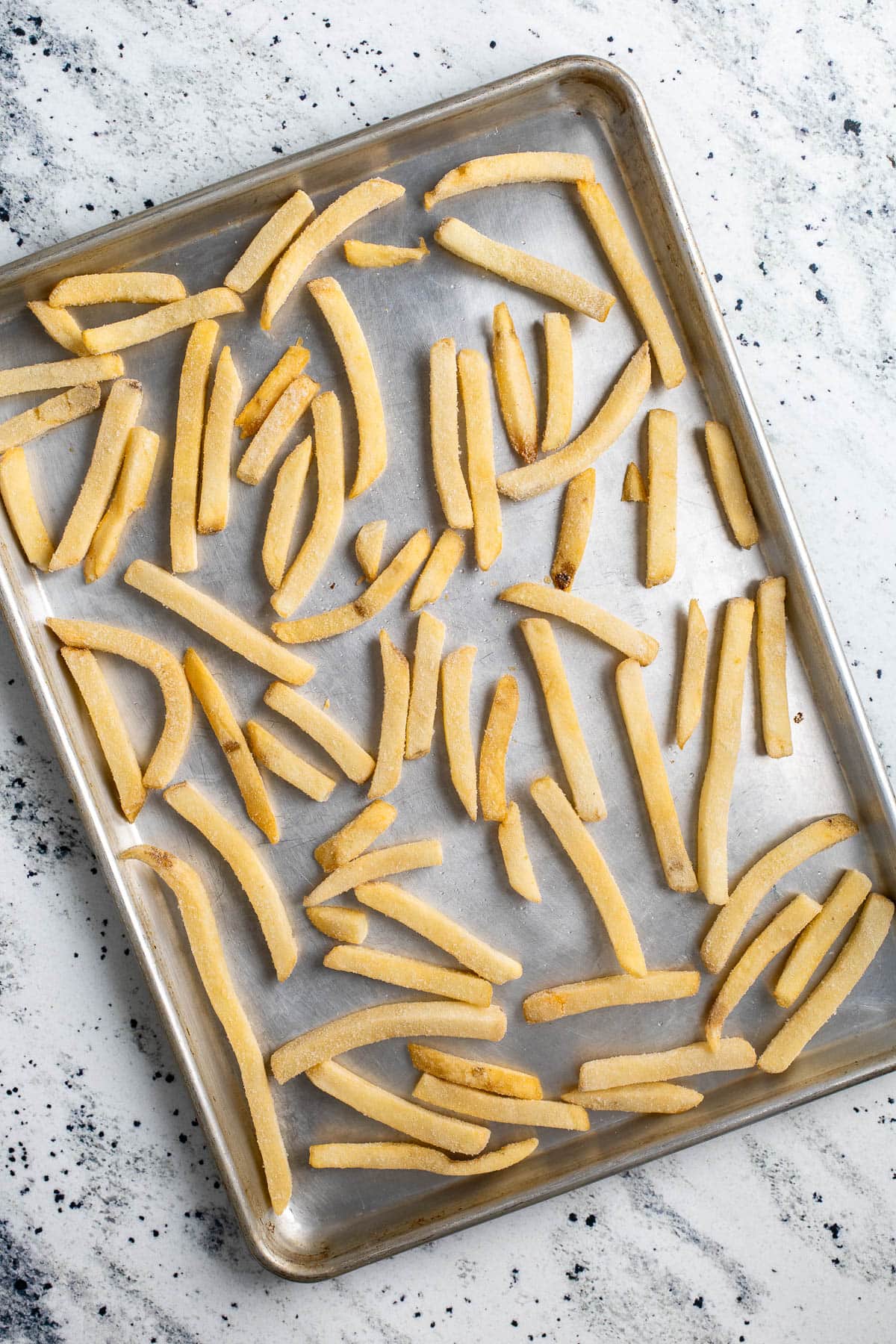 Frozen French fries arranged in a single layer on a sheet pan.