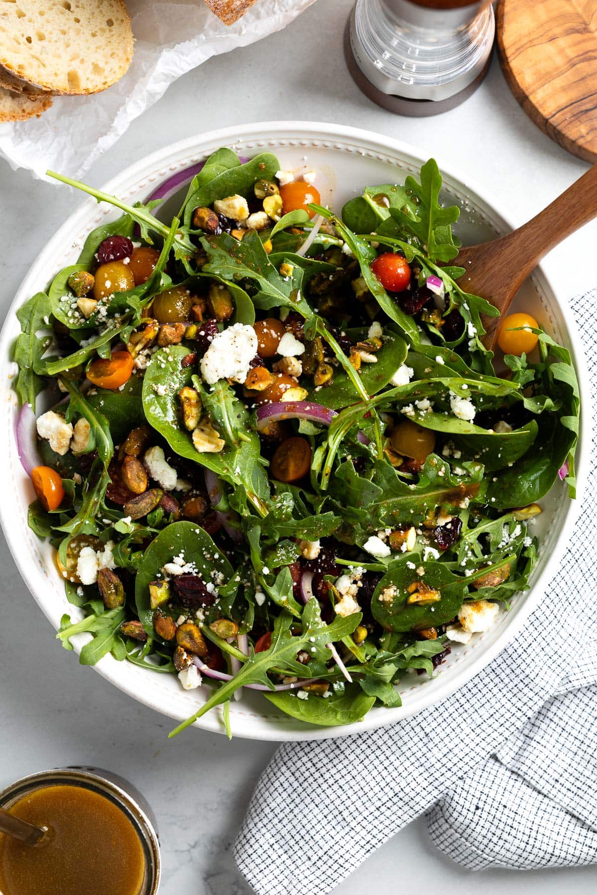 A spinach arugula salad in a serving bowl with a wooden utensil.