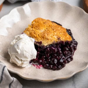 A serving of wild blueberry cobbler on a dessert plate with a scoop of ice cream.