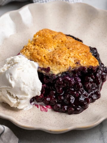 A serving of wild blueberry cobbler on a dessert plate with a scoop of ice cream.
