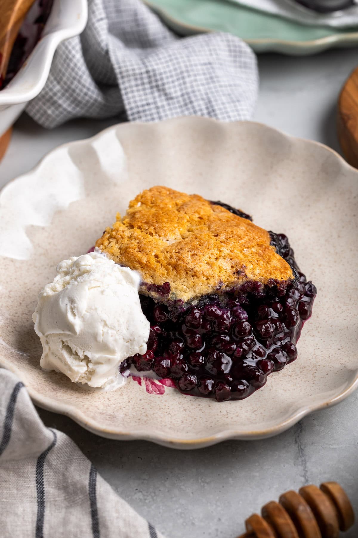 A serving of wild blueberry cobbler on a dessert plate with a scoop of ice cream.