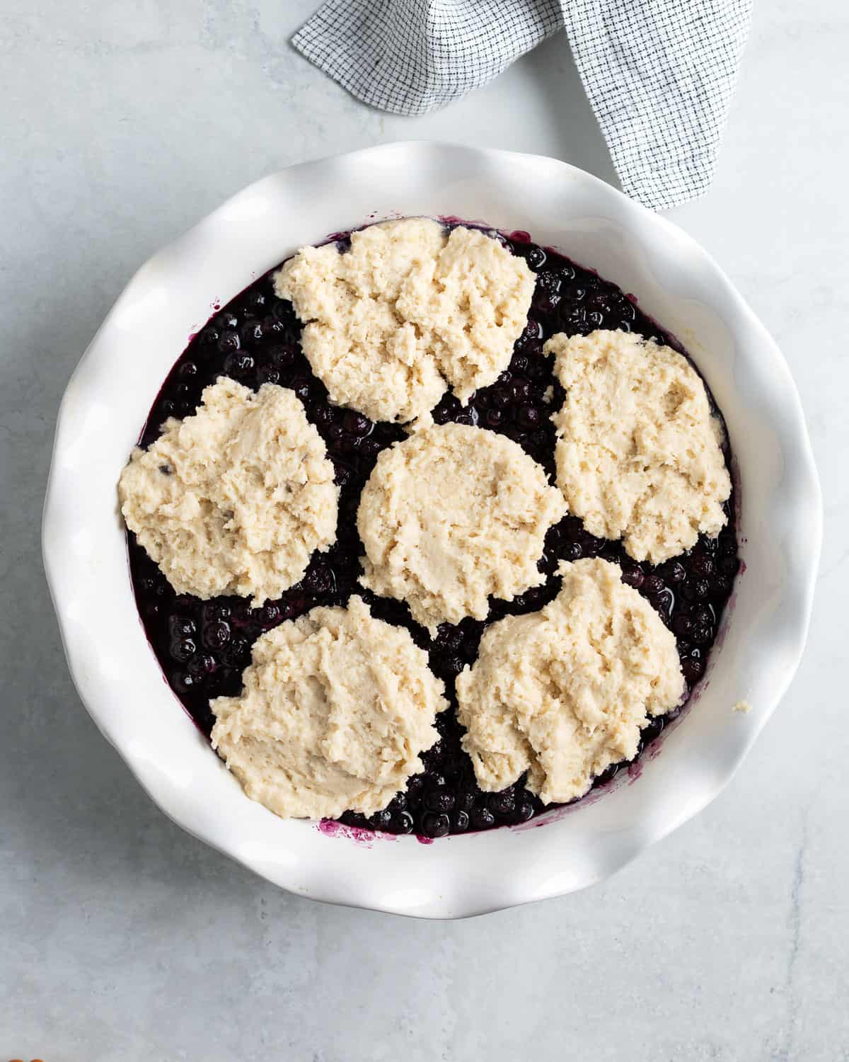 Biscuit cobbler topping arranged on top of the blueberries in the pan.