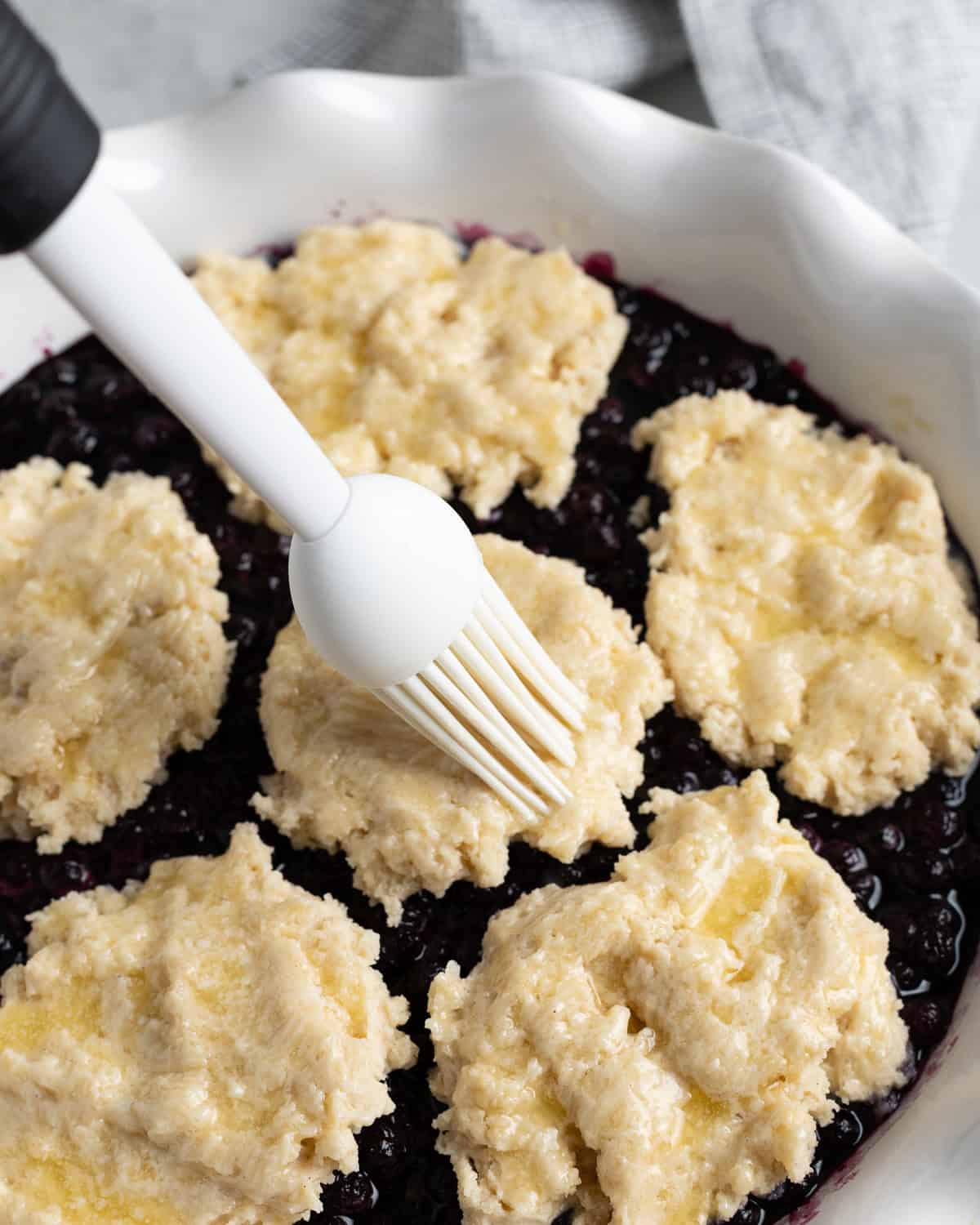 Butter being brushed on the biscuit cobbler topping.
