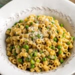 Pasta e piselli in a bowl garnished with shredded Pecorino and cracked pepper.