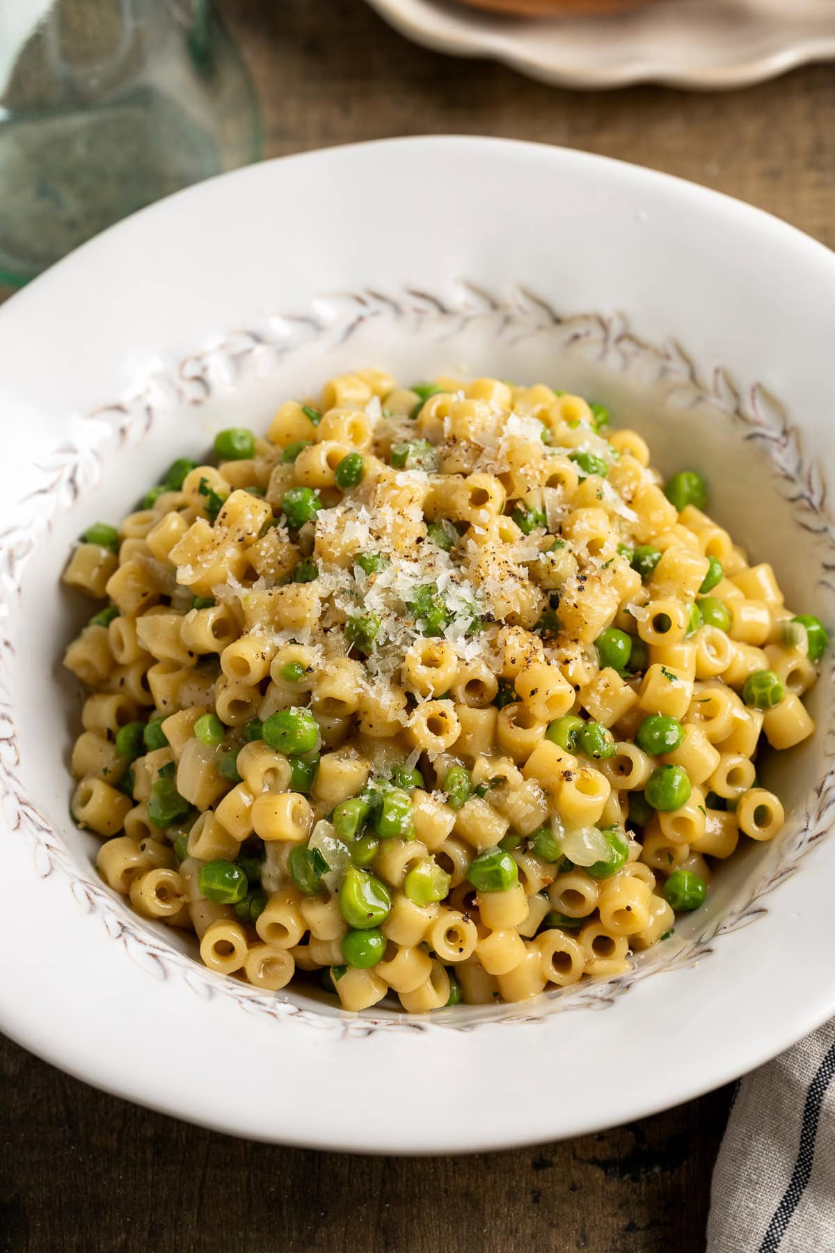 Pasta e piselli in a bowl garnished with shredded Pecorino and cracked pepper.