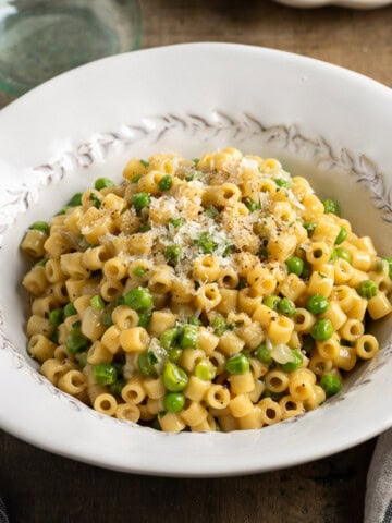 A serving bowl of pasta and peas sprinkled with Pecorino.