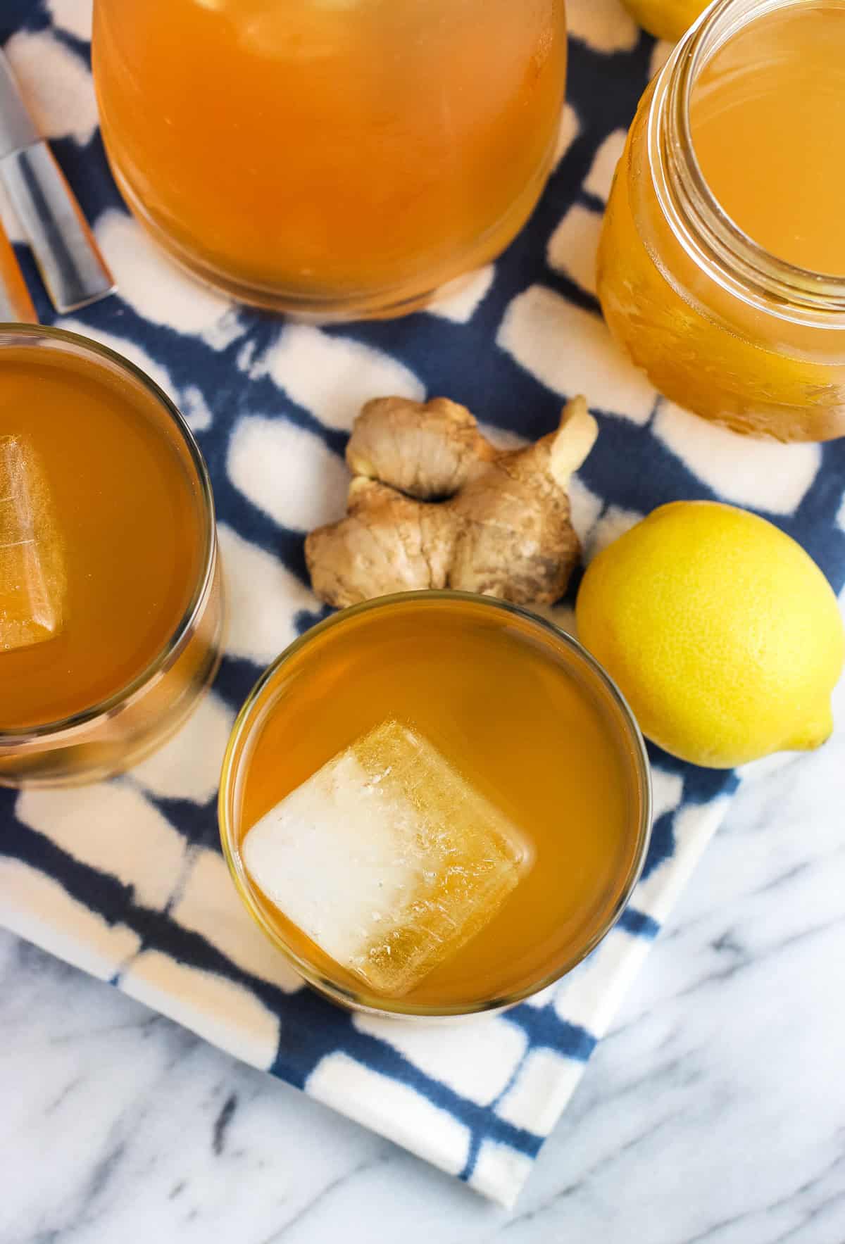 Glasses of iced tea surrounded by a lemon and ginger root.