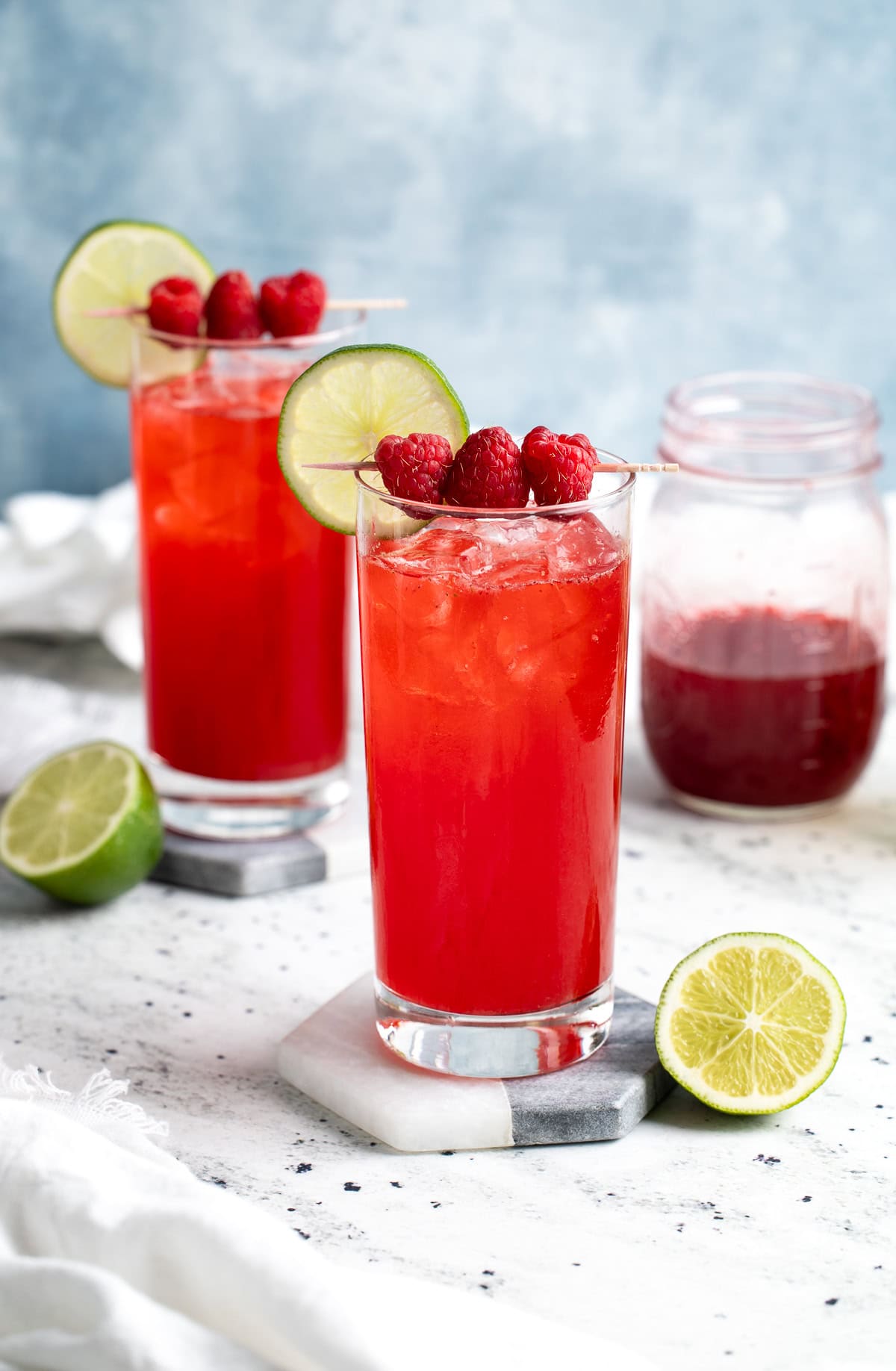 Two drinks in highball glasses garnished with raspberries and lime rounds.