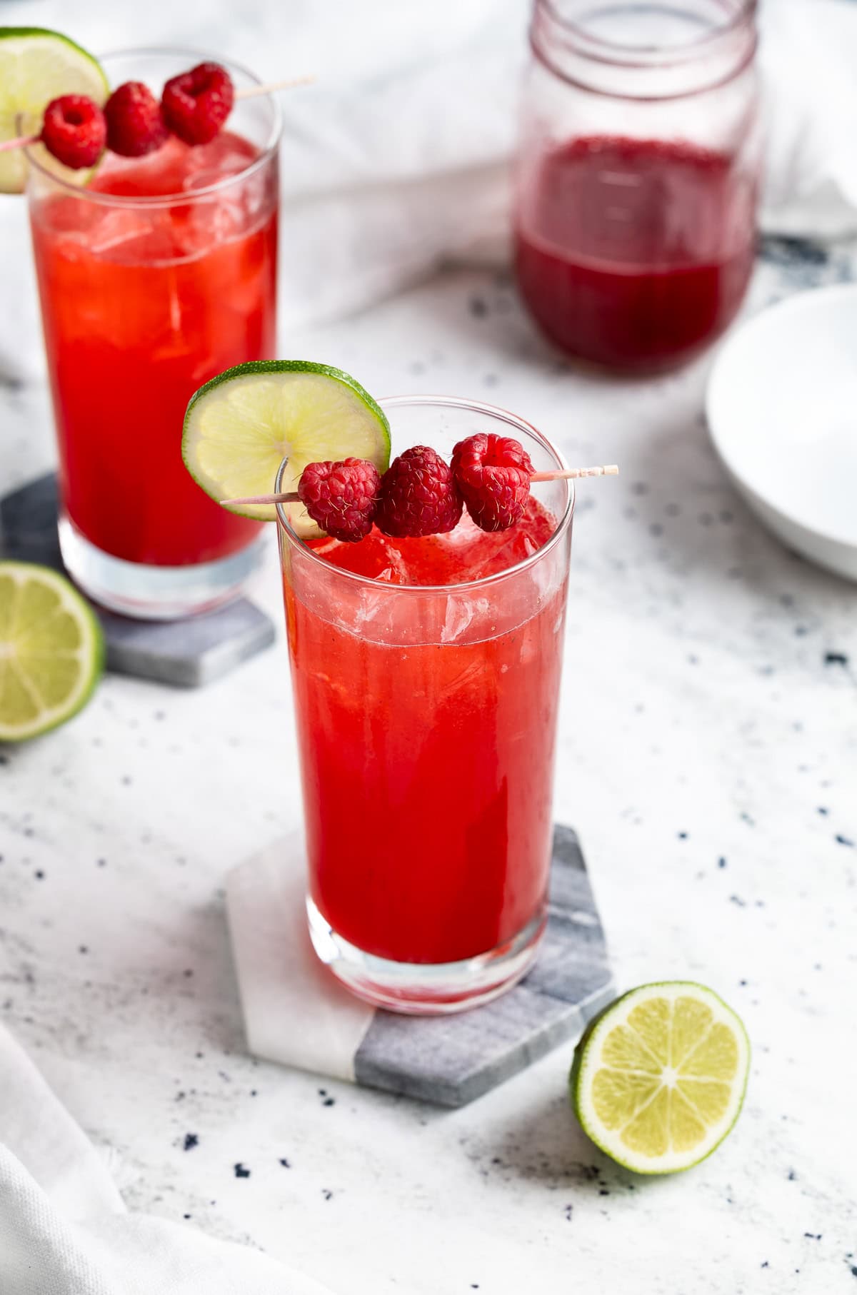 Two raspberry lime rickeys in highball glasses garnished with raspberries and lime rounds.
