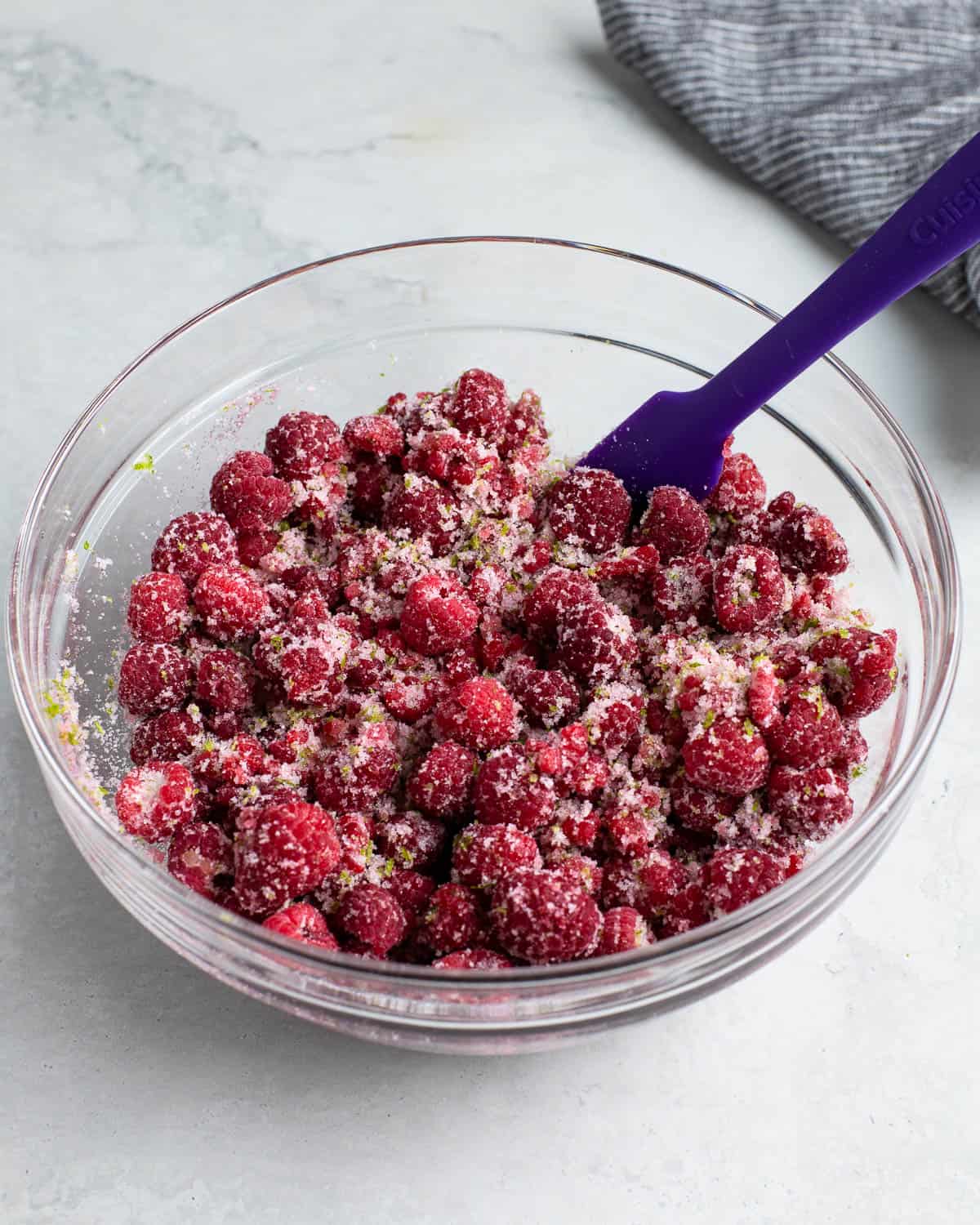 Raspberries in a bowl coated with sugar and lime zest.