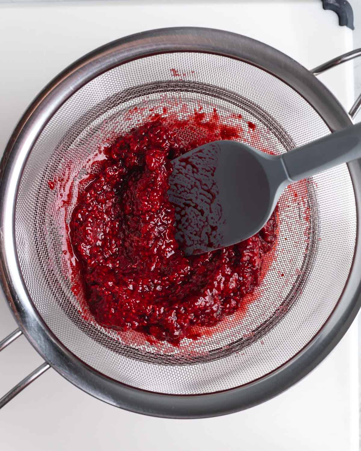 Raspberries being pressed through a sieve to extract the syrup.