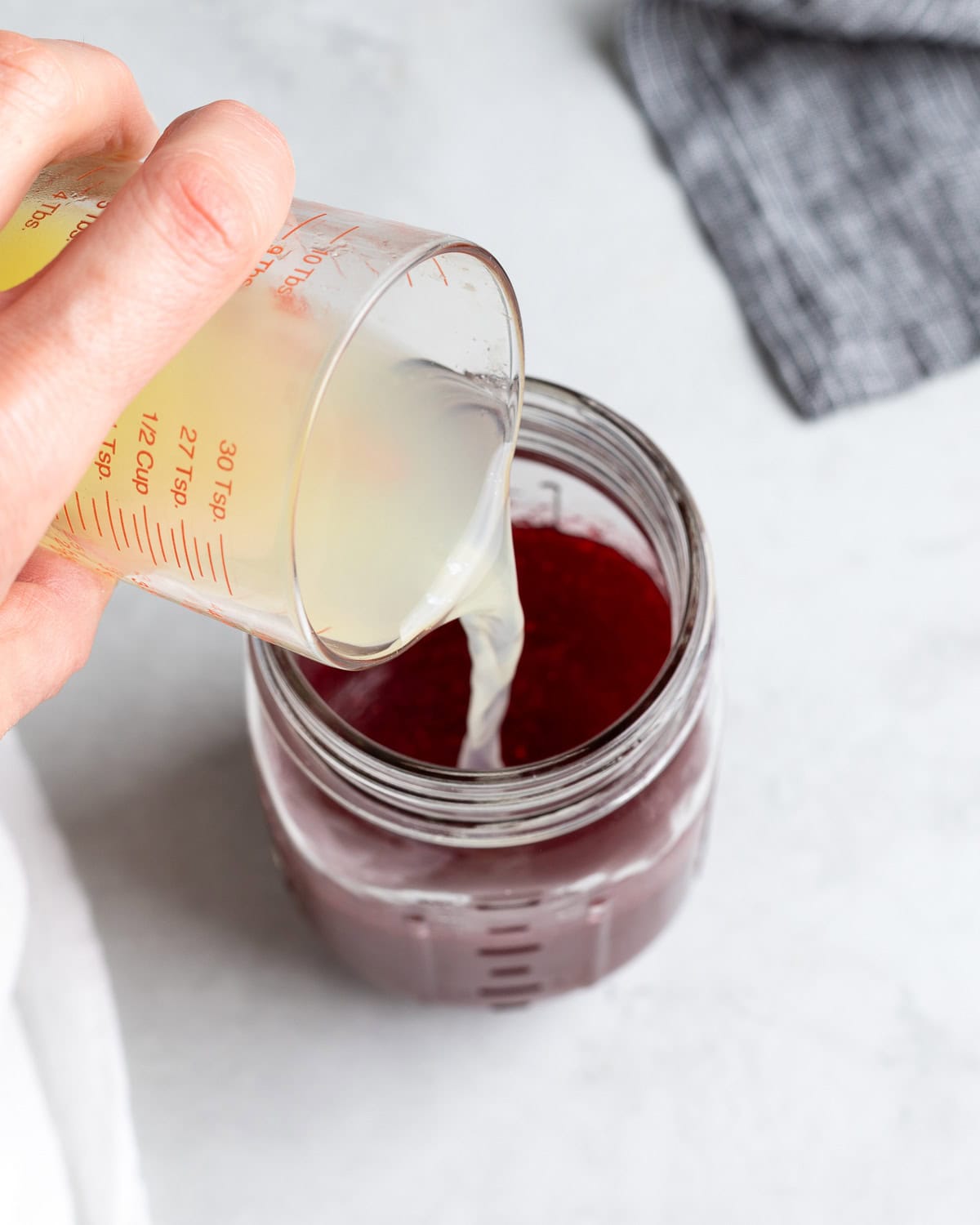 Lime juice being poured into a jar of raspberry syrup.