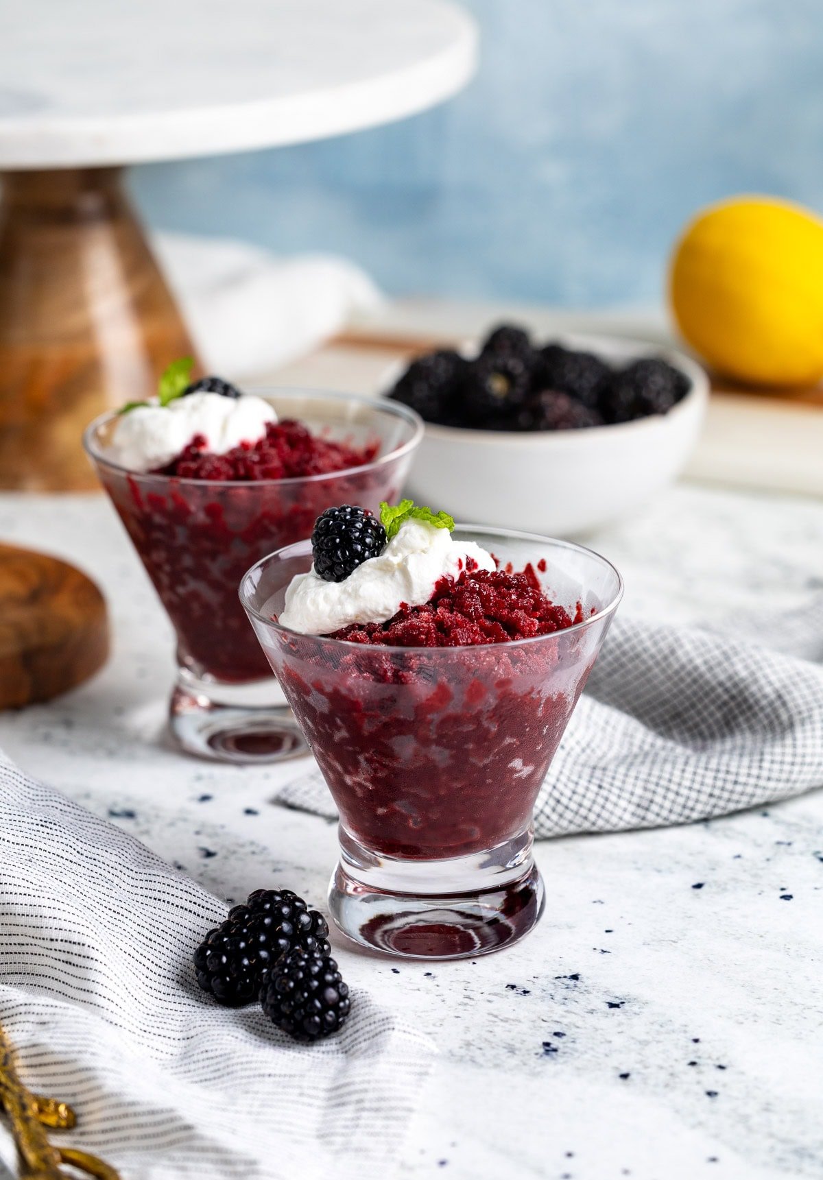 Cups of blackberry granita served with a dollop of whipped cream, whole blackberries, and mint.