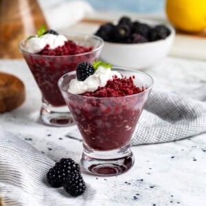 Cups of blackberry granita served with a dollop of whipped cream, whole blackberries, and mint.