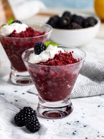Cups of blackberry granita served with a dollop of whipped cream, whole blackberries, and mint.