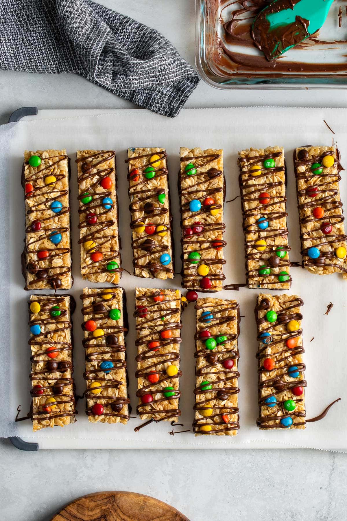 A batch of homemade kudos bars on a cutting board after being drizzled by chocolate.