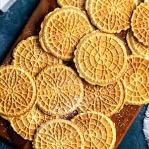 Golden-brown pizzelle dusted with powdered sugar on a wooden board.