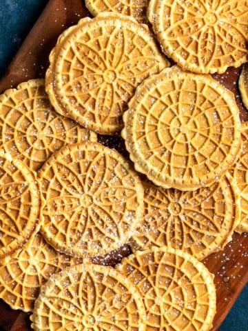 Golden-brown pizzelle dusted with powdered sugar on a wooden board.