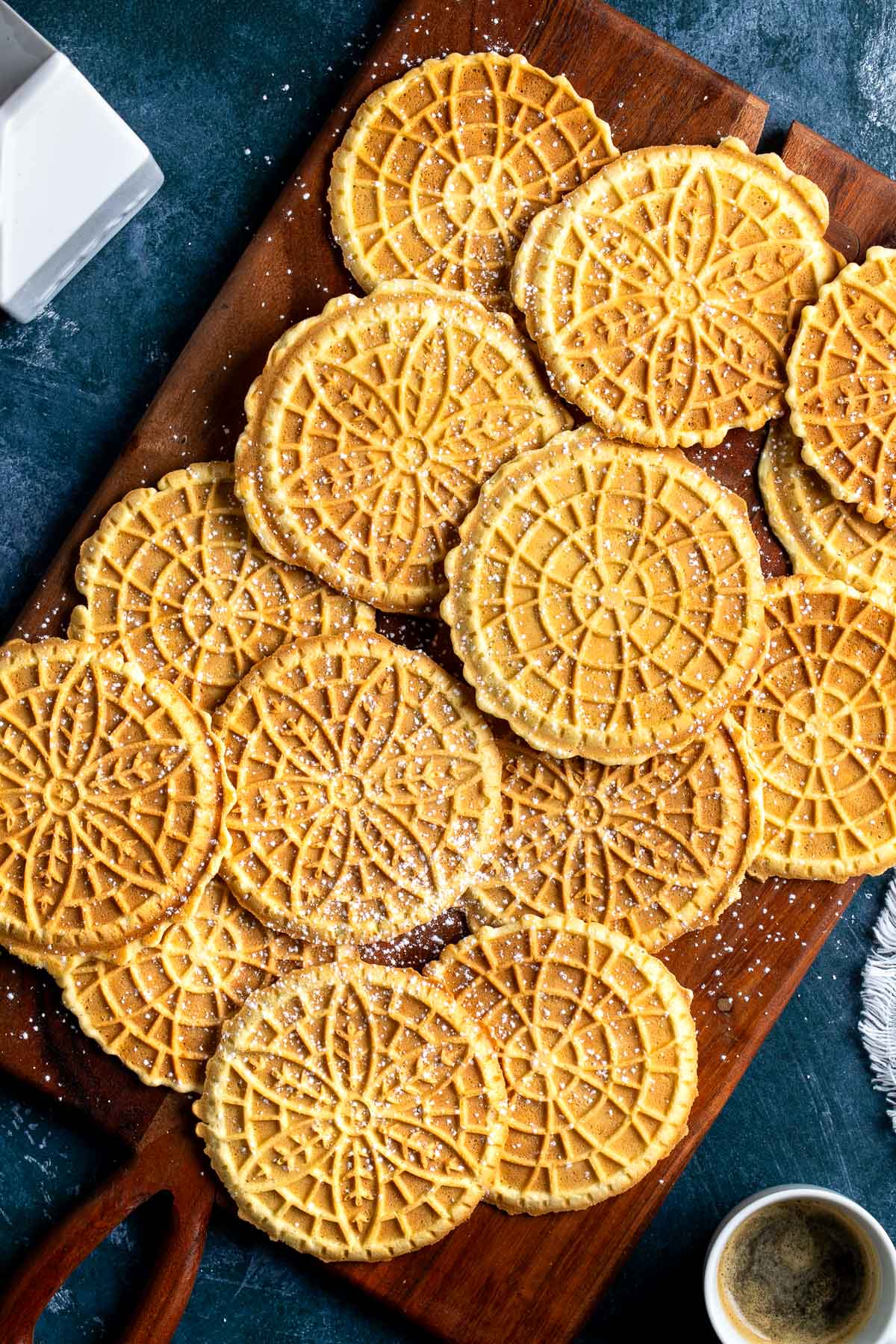 Golden-brown pizzelle dusted with powdered sugar on a wooden board.