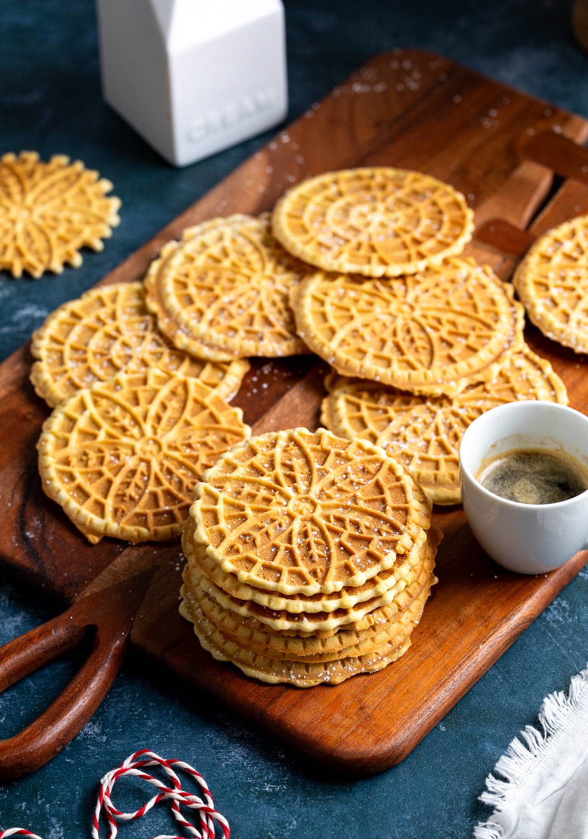 Stacked pizzelle on a wooden serving board with a cup of espresso.