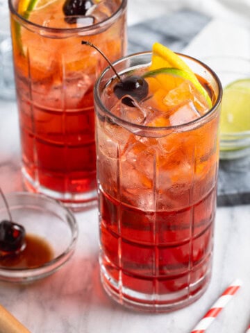 Two Shirley Temple mocktails in tall glasses garnished with fruit.