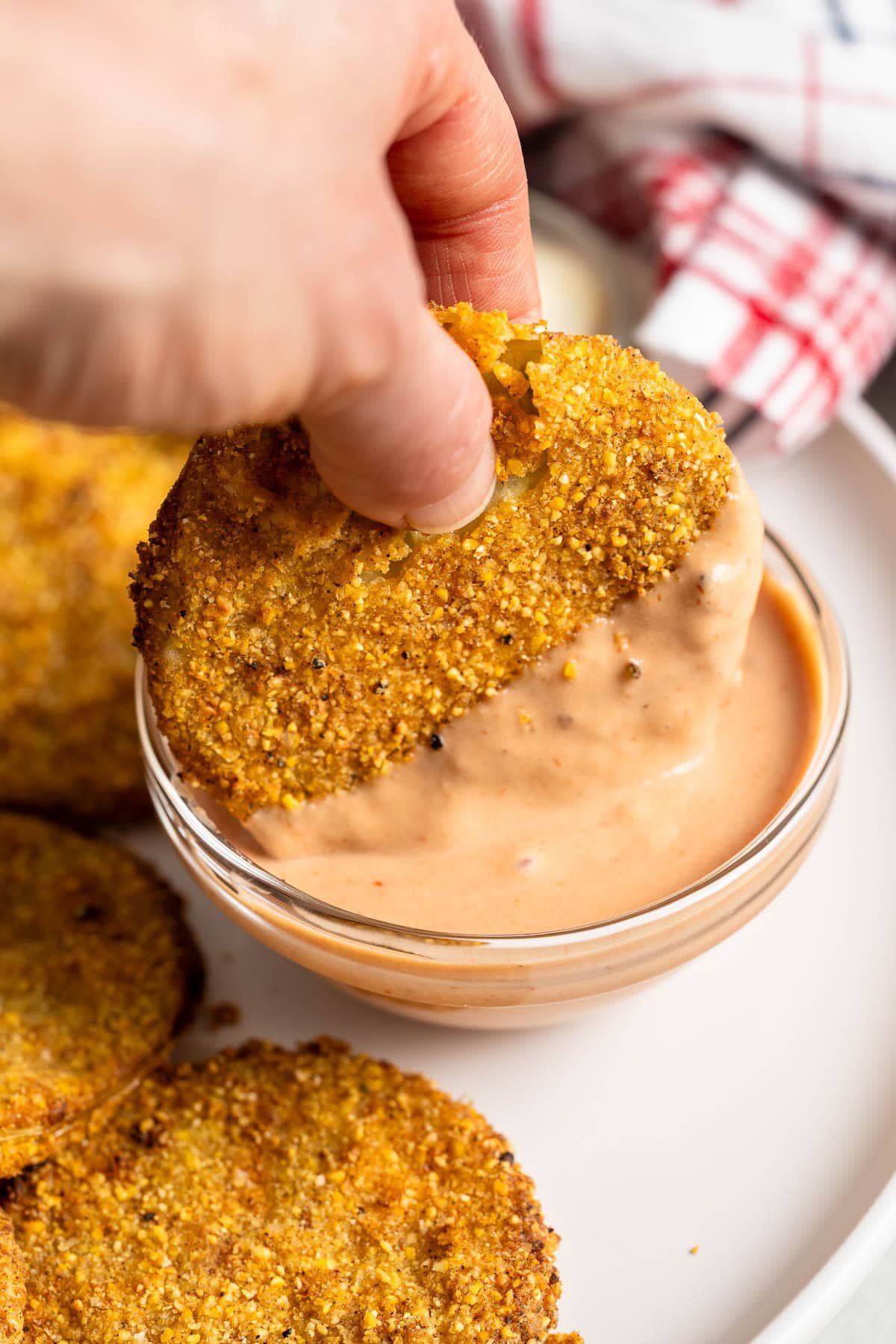 A hand dipping a fried green tomato into a bowl of comeback sauce.