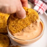 A hand dipping a fried green tomato into a bowl of comeback sauce.