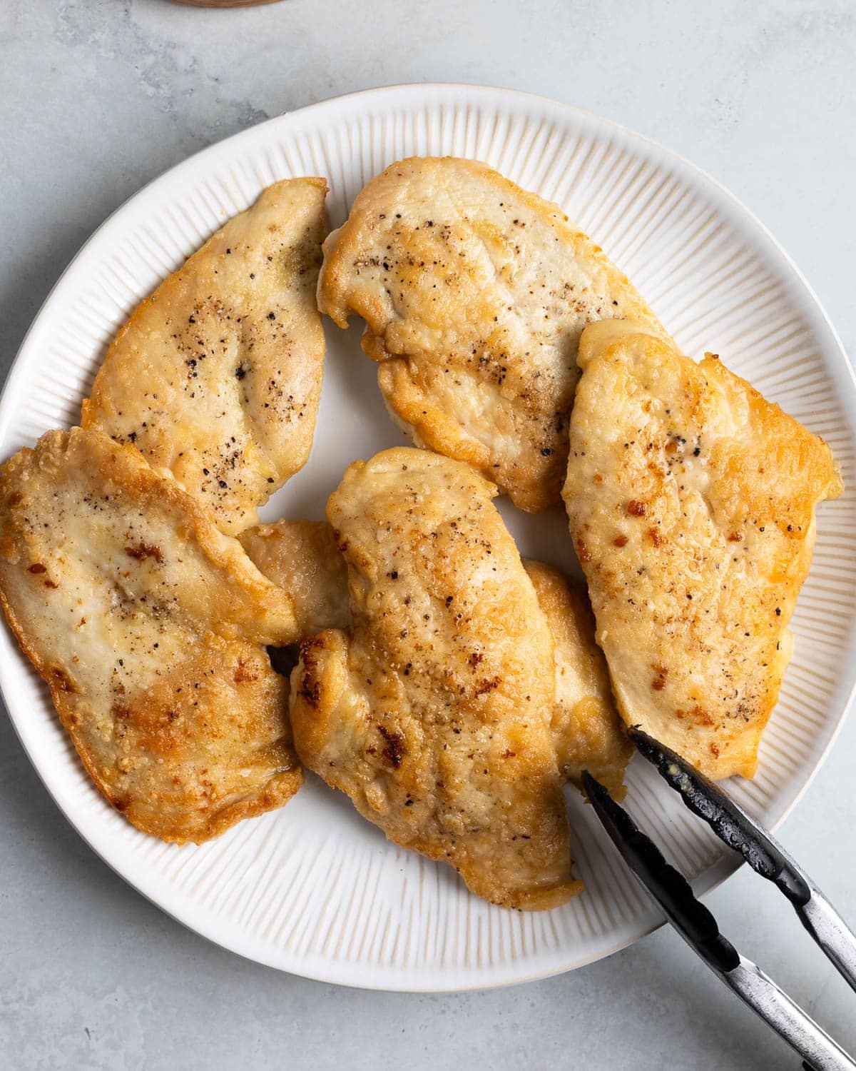 Browned chicken cutlets on a plate with tongs.