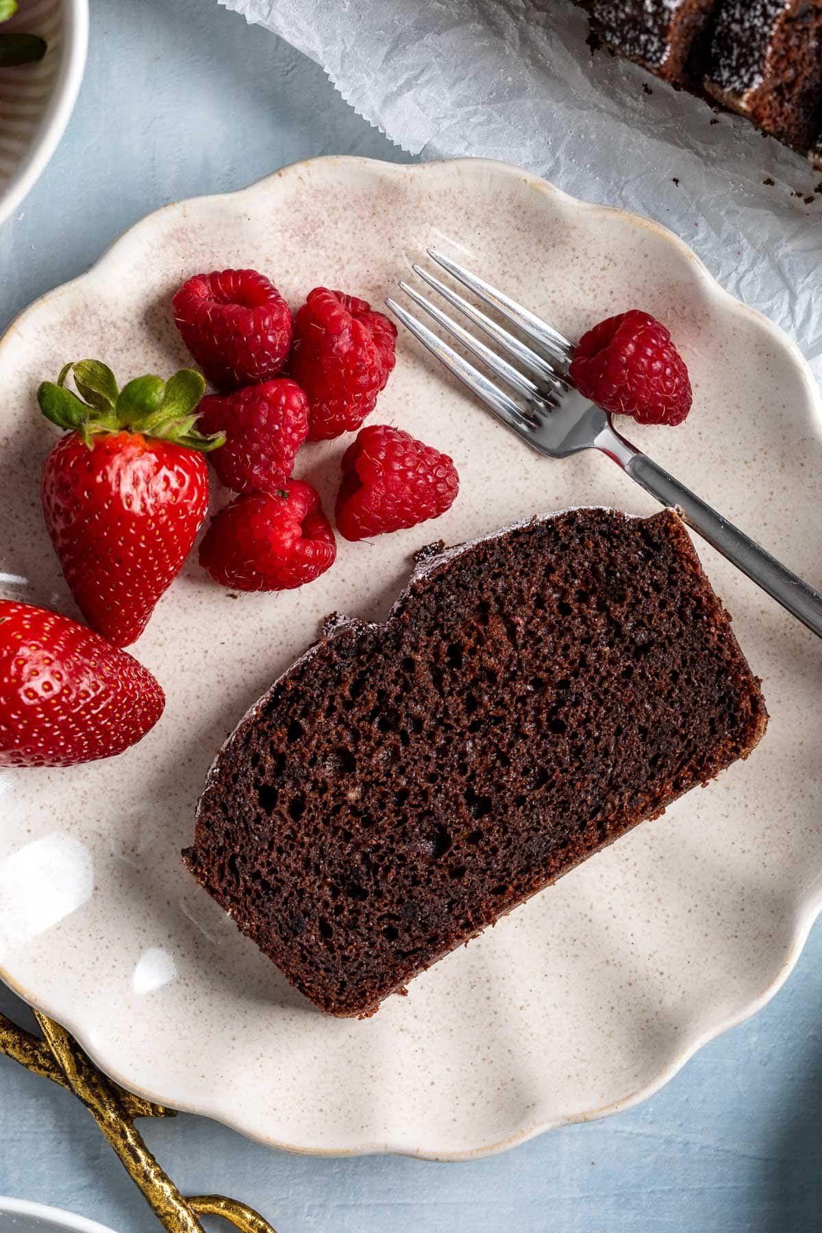 A slice of chocolate yogurt cake on a plate with strawberries and raspberries.