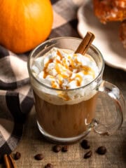 A caramel pumpkin spice latte surrounded by espresso beans and a pumpkin.
