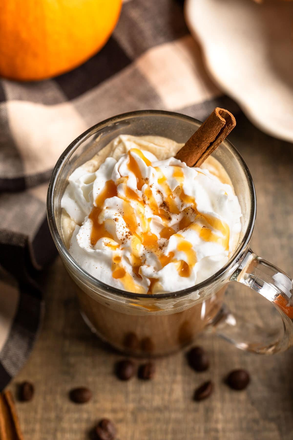 A whipped cream topped caramel pumpkin spice latte in a glass mug.