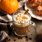 A caramel pumpkin spice latte surrounded by espresso beans and a pumpkin.