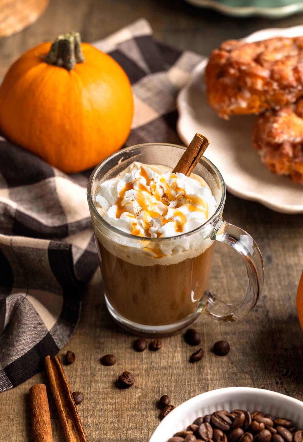 A caramel pumpkin spice latte surrounded by espresso beans and a pumpkin.