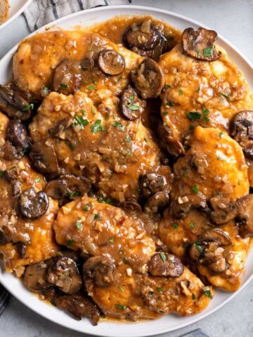 A platter of chicken marsala covered in mushrooms and sauce.