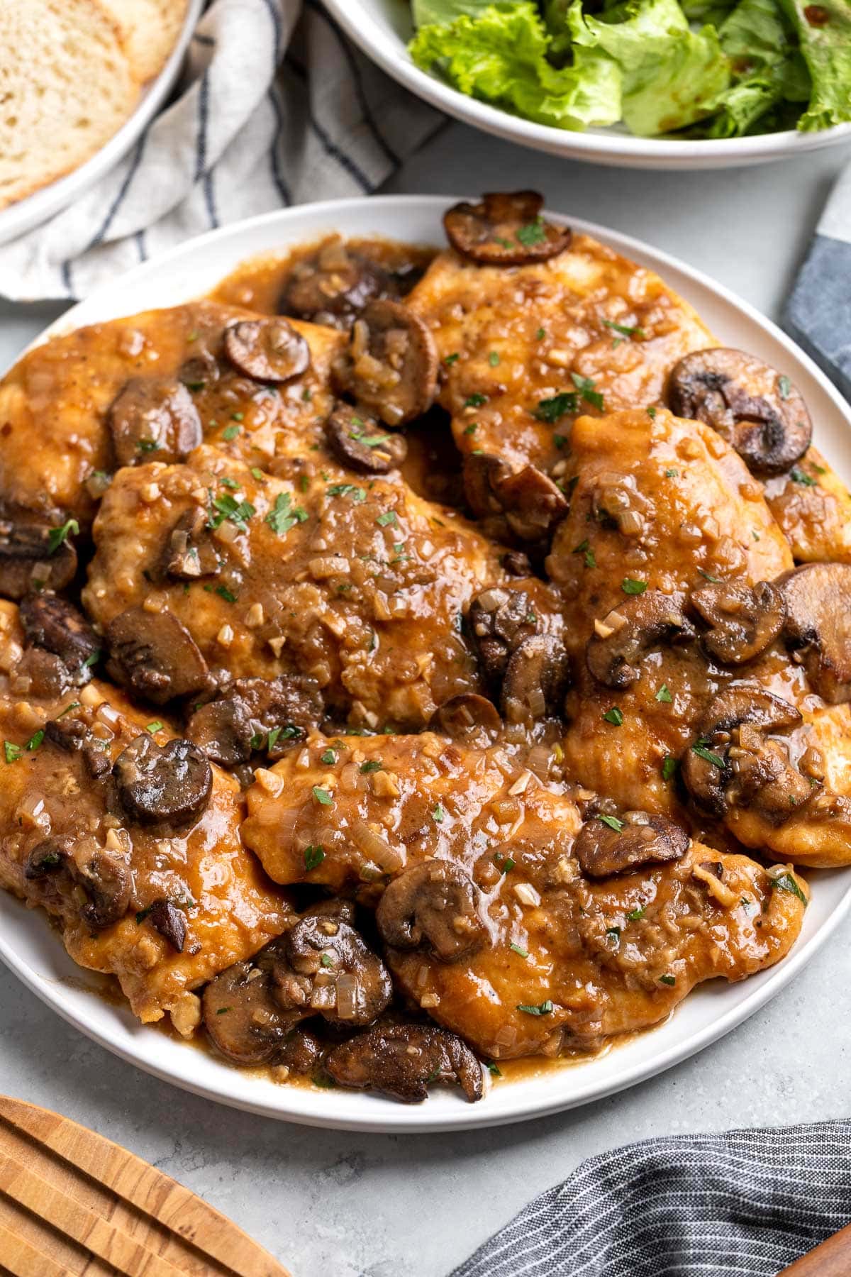 Six chicken marsala cutlets on a serving plate with thickened sauce and mushrooms.