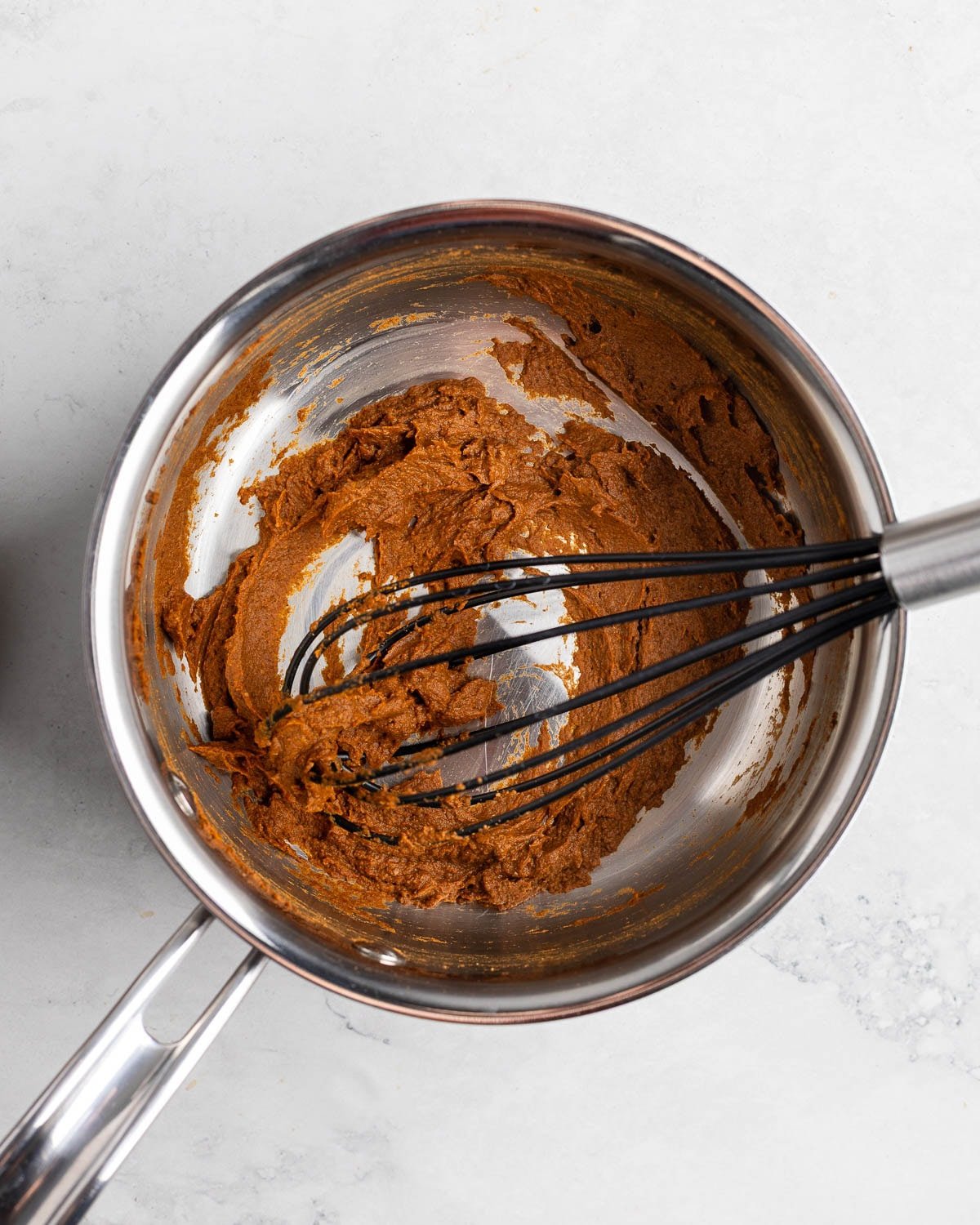 Pumpkin puree and spices combined in a pan with a whisk.