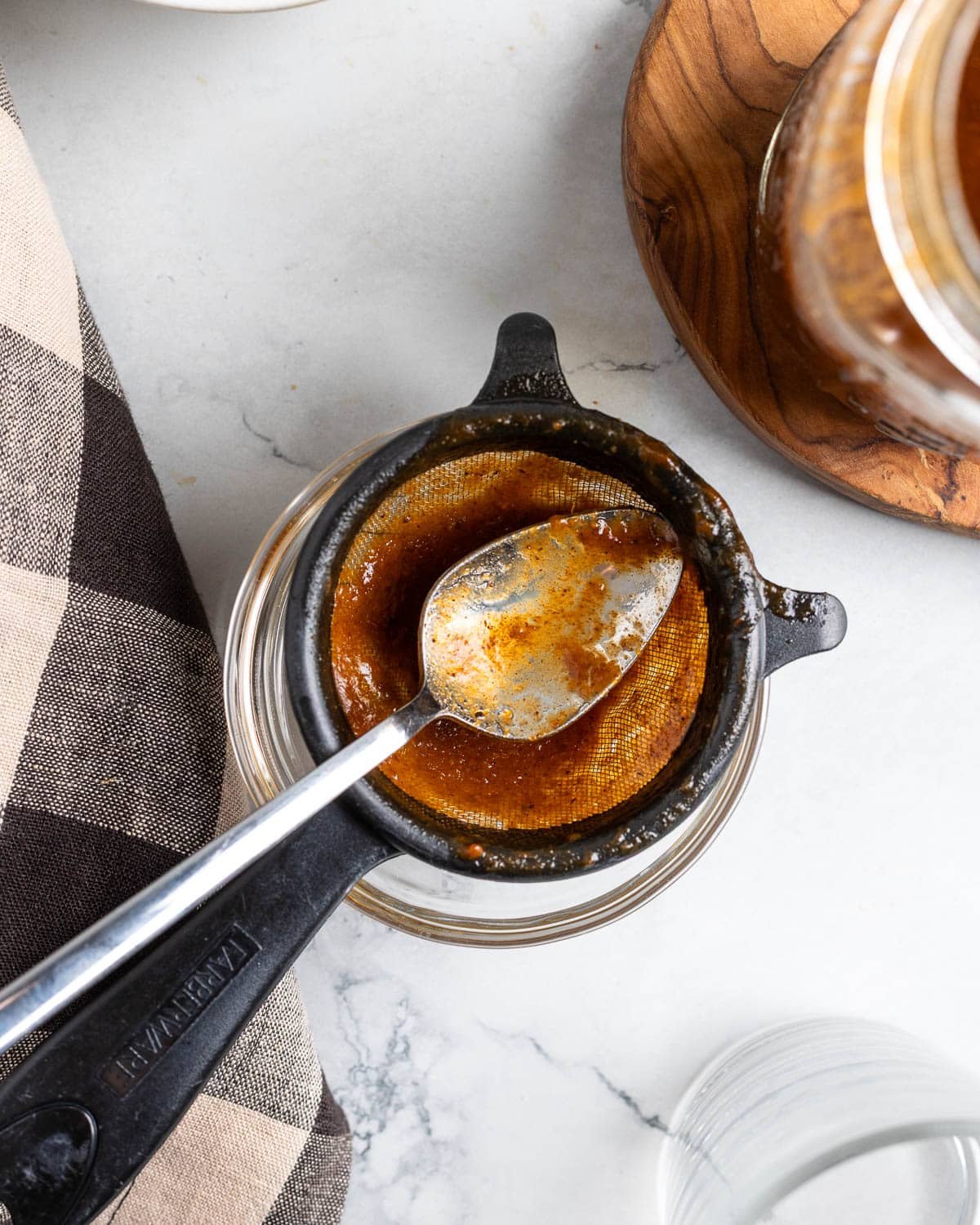 A spoon and strainer in a bowl after straining the pumpkin spice syrup.