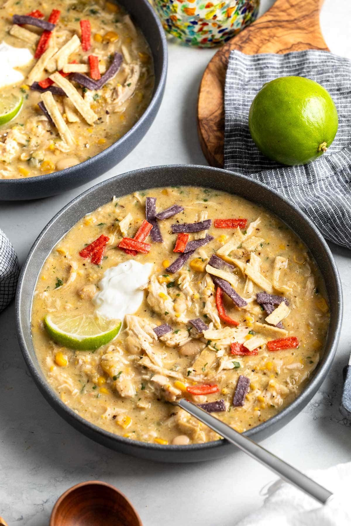 Serving bowls of white chicken chili topped with tortilla strips, sour cream, and a lime wedge.