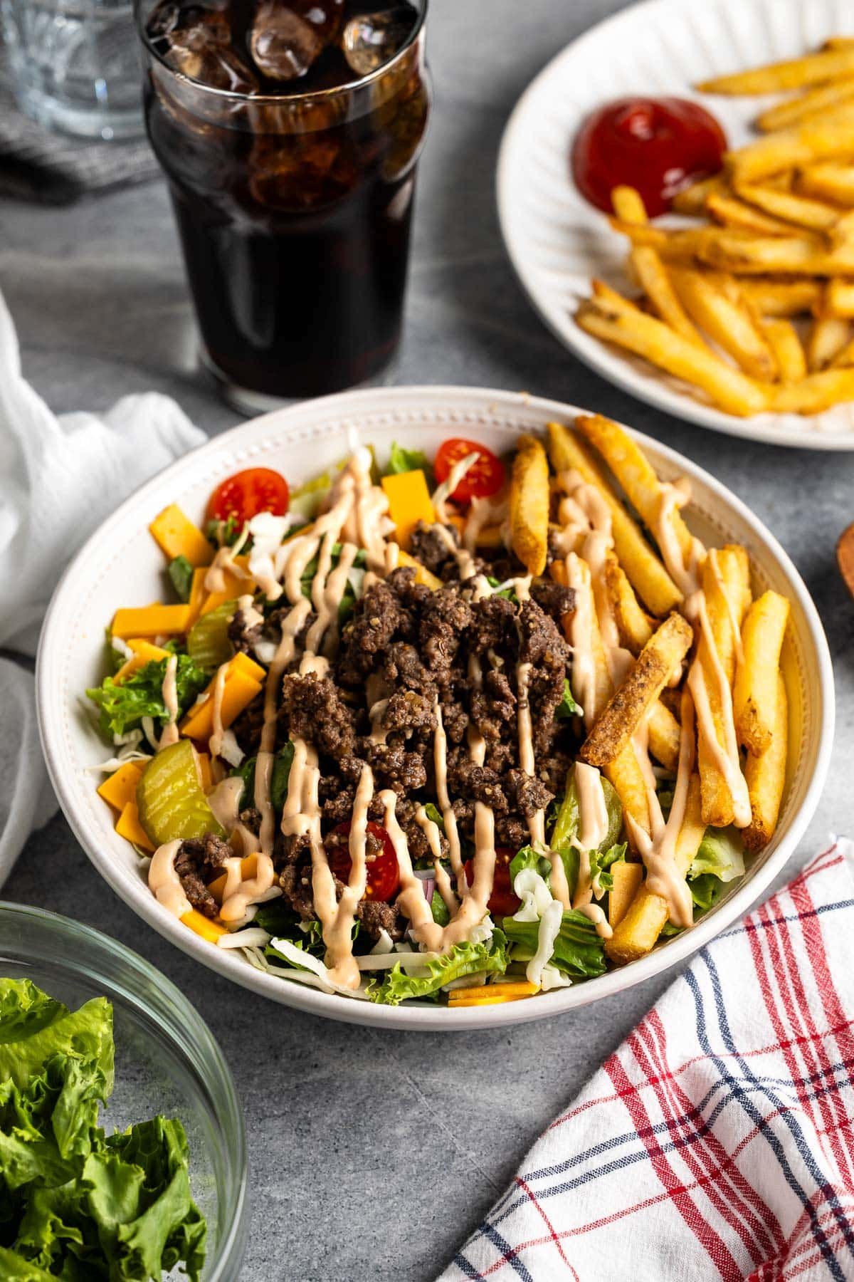 A big bowl of lettuce and coleslaw mix topped with burger bowl elements - beef, pickles, tomatoes, cheese, onion, and burger sauce.