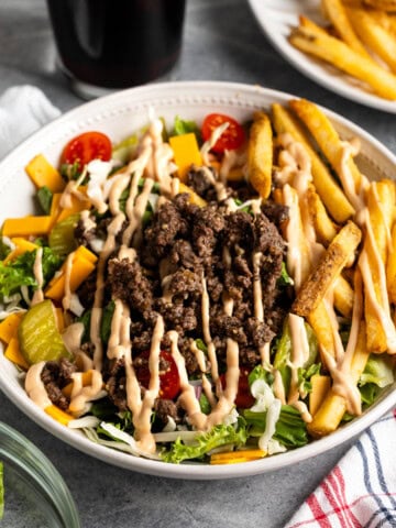 A big bowl of lettuce and coleslaw mix topped with burger bowl elements - beef, pickles, tomatoes, cheese, onion, and burger sauce.