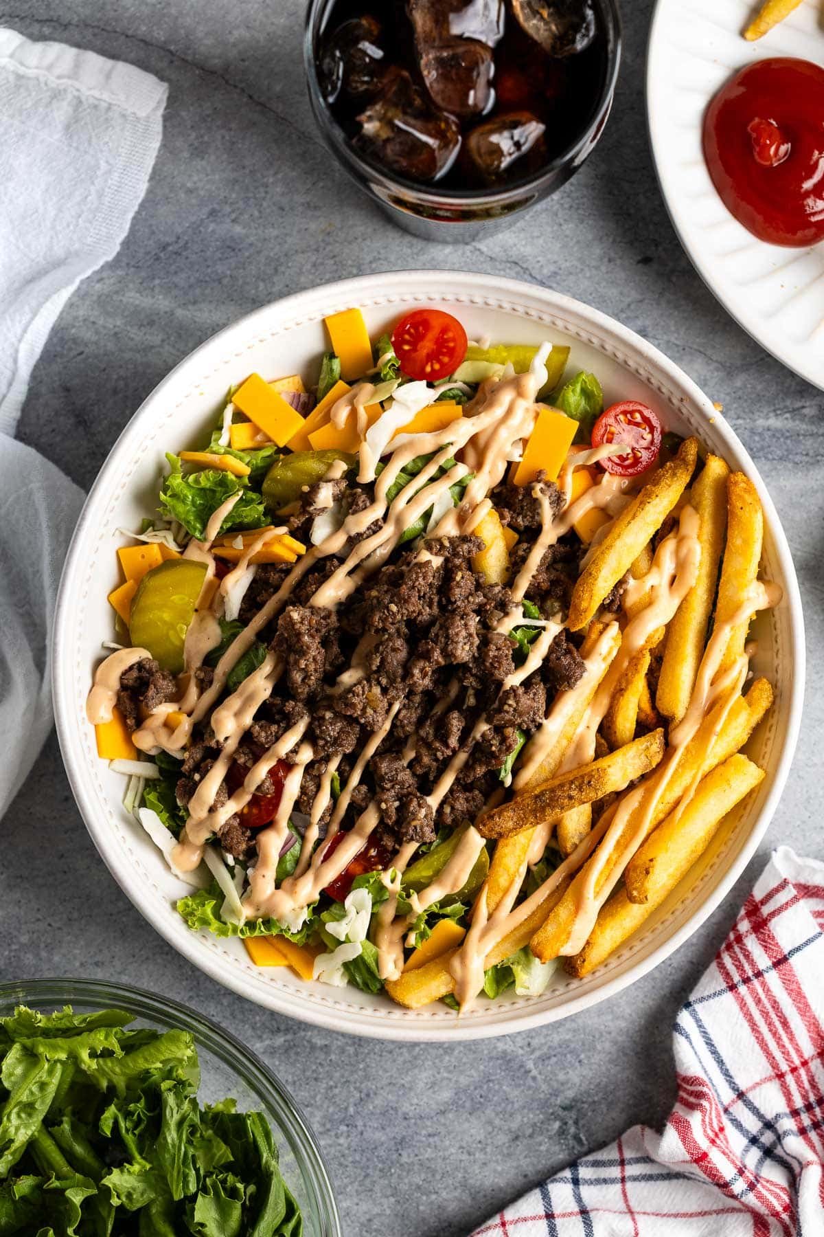 A weeknight burger bowl with all the fixings next to an ice-filled glass of crispy soda.