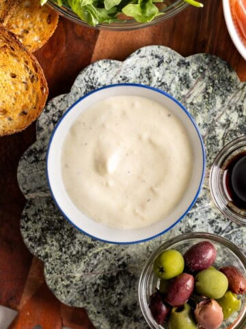 A bowl of lemon aioli surrounded by toasted bread, prosciutto, arugula, olives and balsamic.