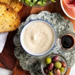 A bowl of lemon aioli surrounded by toasted bread, prosciutto, arugula, olives and balsamic.