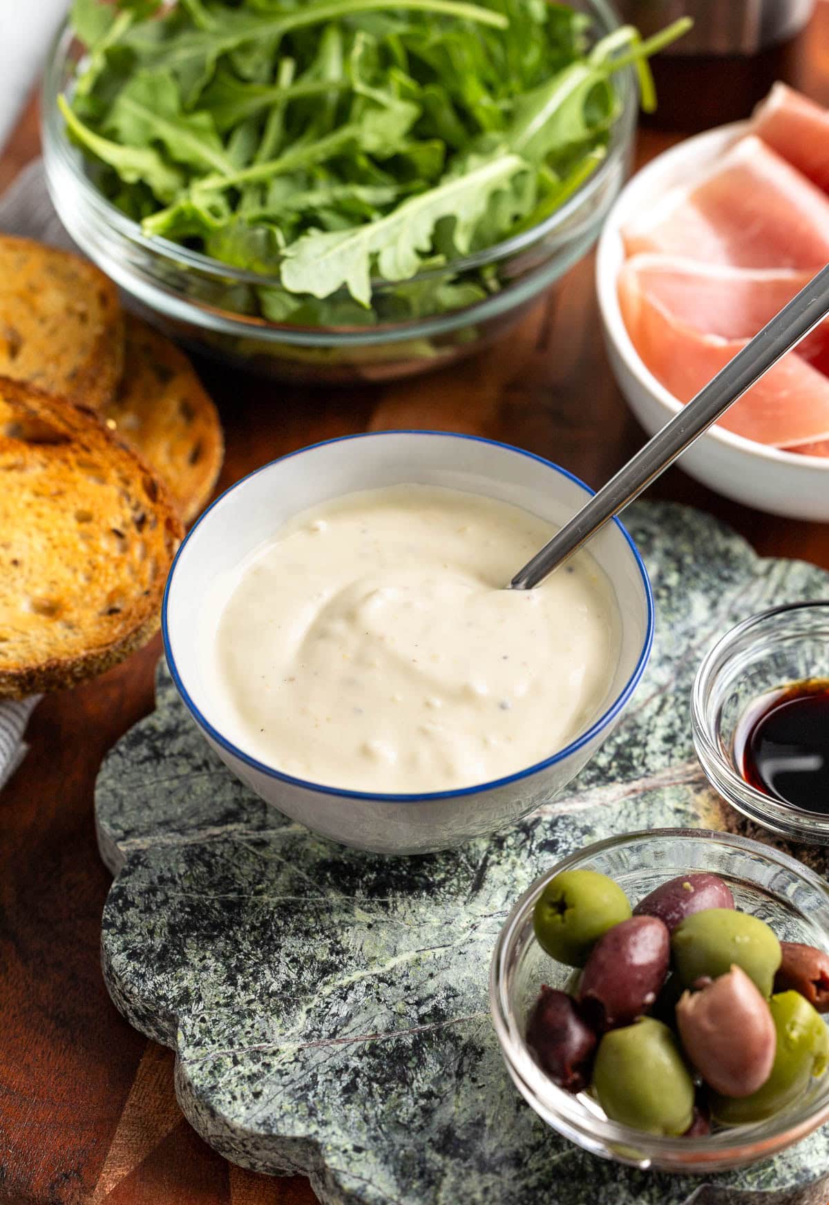 Lemon aioli in a bowl with a spoon in it on a serving board.