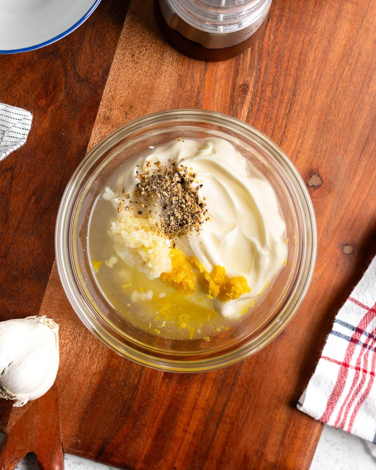 Mayo and the rest of the aioli ingredients added to a glass bowl.