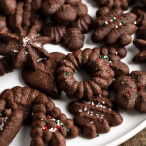 Wreaths, trees, and various other shapes of chocolate spritz cookies, some topped with sprinkles.