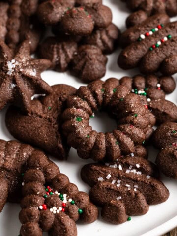 Wreaths, trees, and various other shapes of chocolate spritz cookies, some topped with sprinkles.