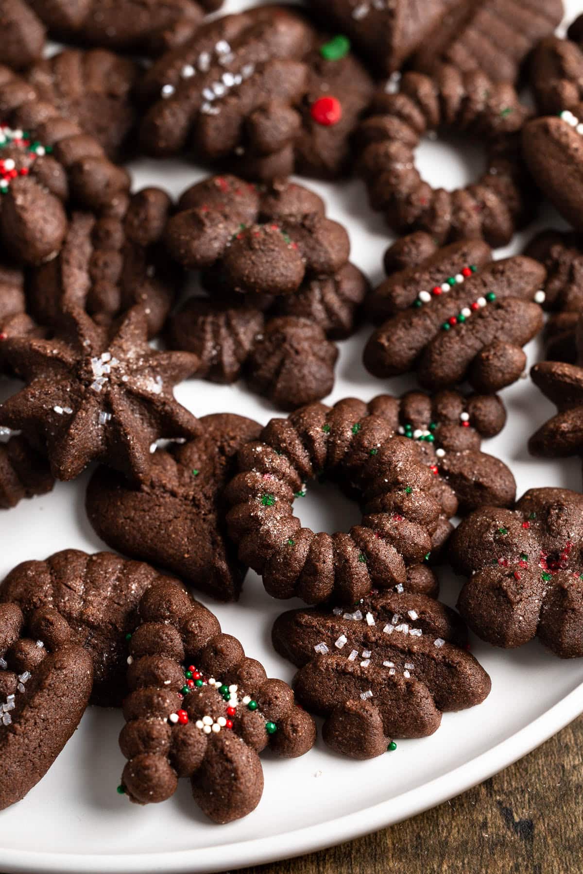 Wreaths, trees, and various other shapes of chocolate spritz cookies, some topped with sprinkles.