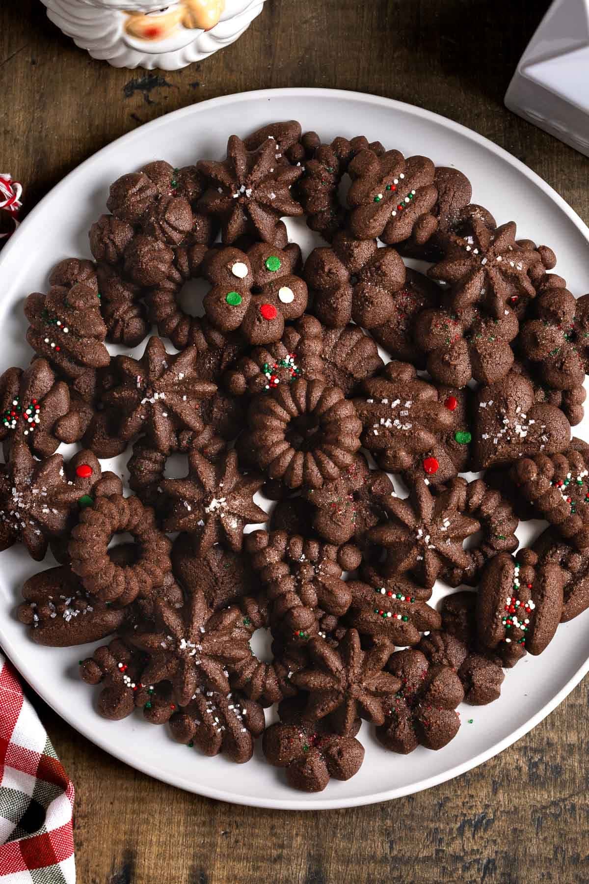 Wreaths, trees, stars, and other shaped chocolate spritz cookies, some topped with sprinkles.